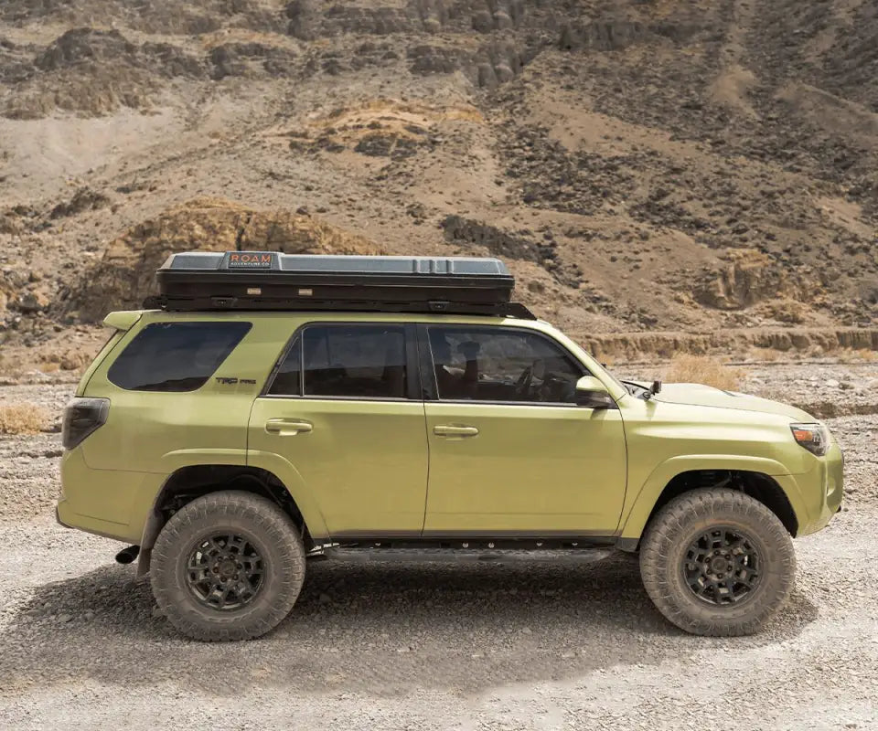 Side view of a Toyota 4Runner with Prinsu Roof Rack and rooftop tent, driving through rugged terrain, showcasing versatility.