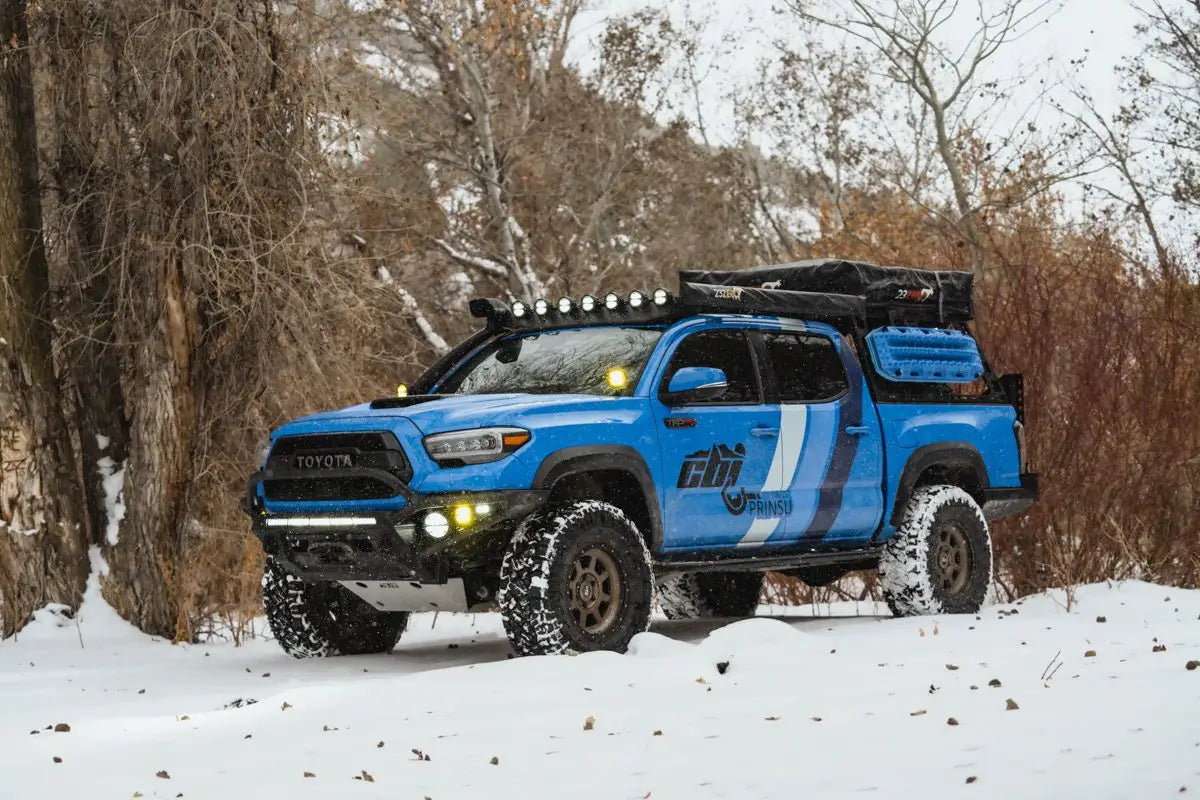 Toyota Tacoma with Prinsu Cab Rack in snowy conditions, featuring mounted cargo and rugged off-road setup.