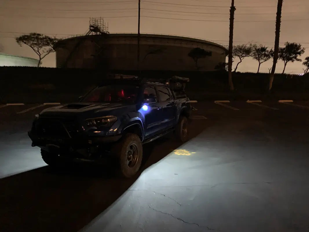 Blue Tacoma parked at night with Puddle Pods LED lights illuminating the ground for enhanced safety.