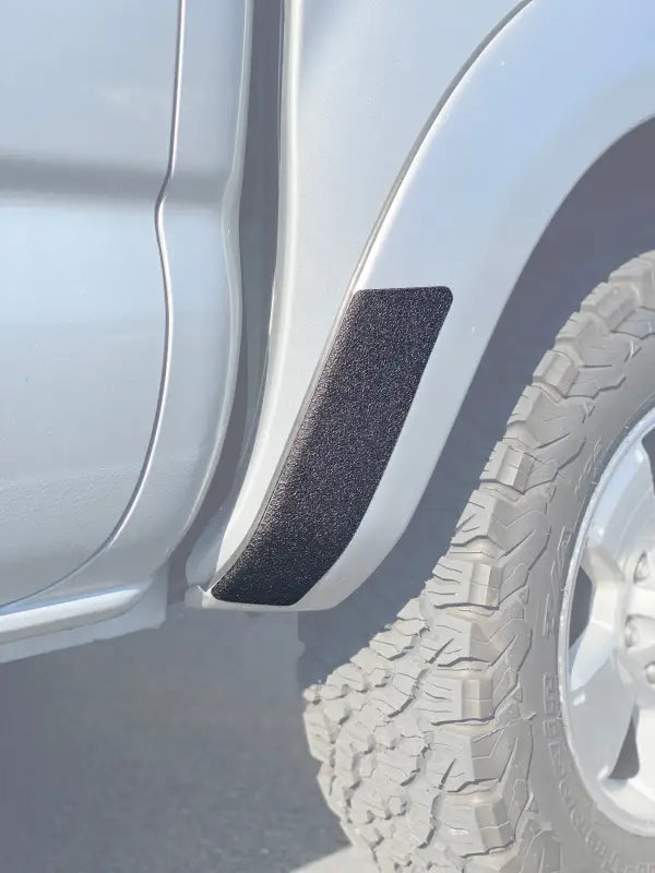 Black textured rear fender protection overlay installed on a silver 2005-2015 Toyota Tacoma, enhancing durability and style.