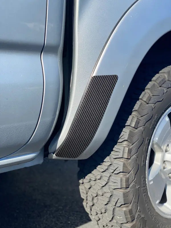 Carbon fiber rear fender protection overlay installed on a silver 2005-2015 Toyota Tacoma, offering a sleek and durable finish.