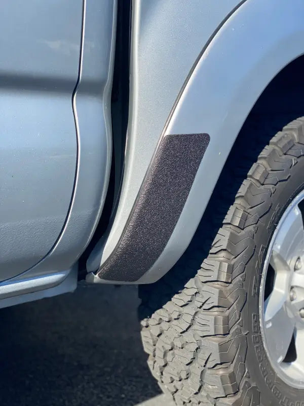 Close-up of black textured rear fender overlay on a 2005-2015 Toyota Tacoma, showcasing precise fit and rugged design.