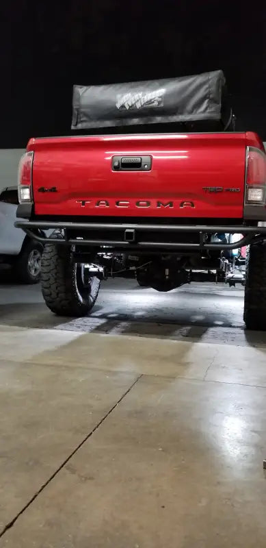 2016+ Tacoma Tube Bumper - High Clearance installed on a red Toyota Tacoma, showcasing a rugged rear design with hitch receiver and light tabs.