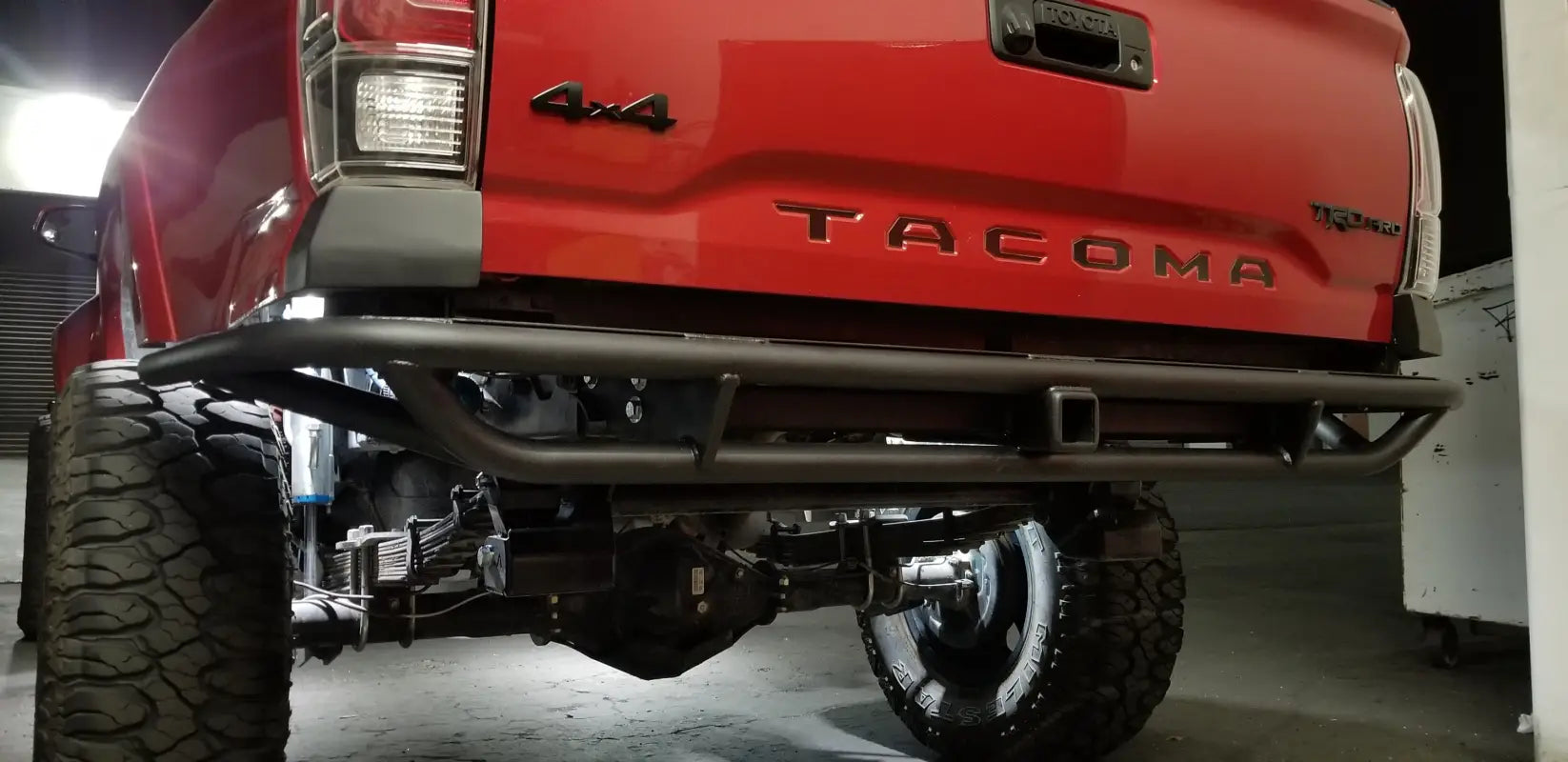 Close-up view of 2016+ Tacoma Tube Bumper - High Clearance on a red Toyota Tacoma, highlighting its durable construction and bed reinforcement.