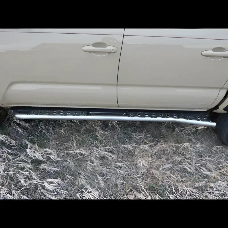 Side profile of a 2016+ Tacoma with bolt-on rock sliders in bare steel. Designed for off-road durability and easy installation.