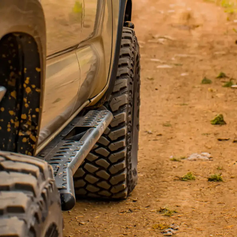 Close-up of Tacoma rock sliders on a 2016+ model driving on a dirt trail. Durable bolt-on sliders with removable step plates.