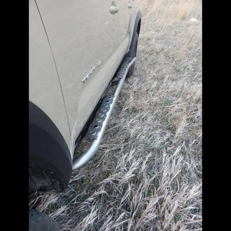 Tacoma rock sliders in bare steel finish installed on a 2016+ model. Designed for easy bolt-on installation and off-road protection.