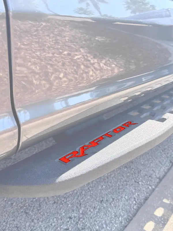 Red RAPTOR lettering on a running board emblem overlay for Ford Raptor