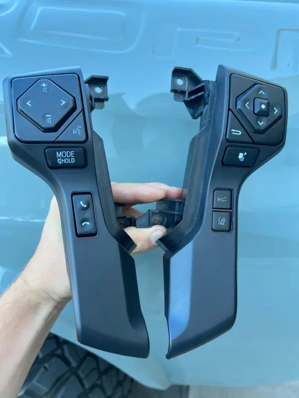 Hand holding steering wheel blackout surround inserts with buttons, designed for 2016-2023 Toyota Tacoma models.