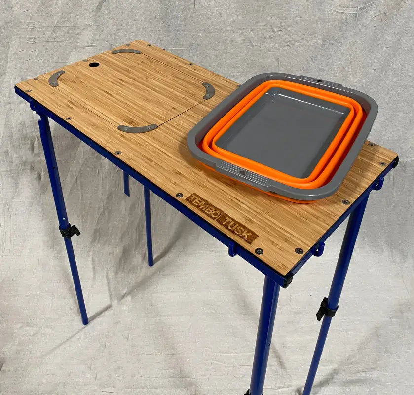 TemboTusk Camp Table featuring collapsible orange basin and bamboo surface with removable cover. Compact and easy to set up.