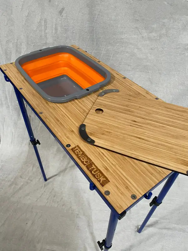 TemboTusk Camp Table Kit with collapsible orange basin, bamboo top, and adjustable blue legs. Durable and portable for outdoor use.