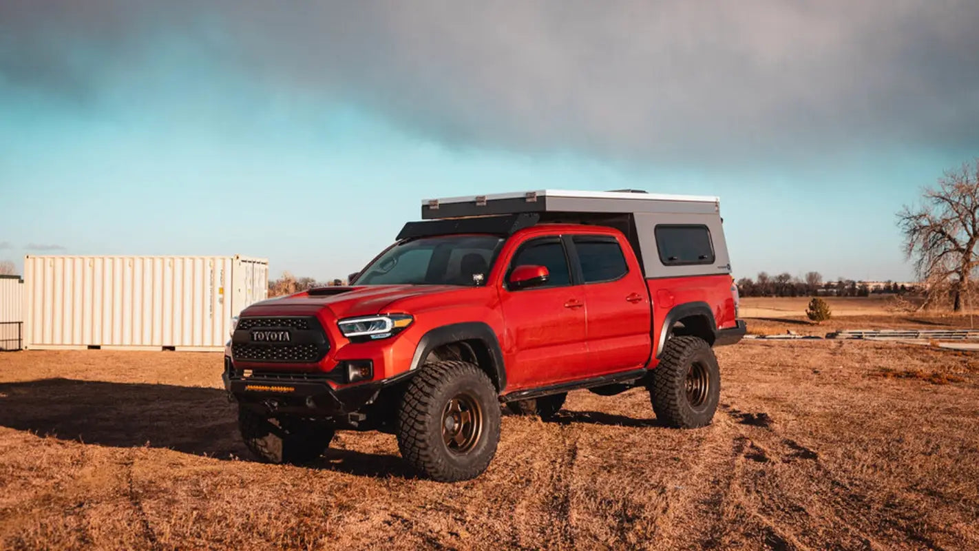 Red Toyota Tacoma with Animas roof rack and camper setup in an open field, designed for versatile storage solutions.