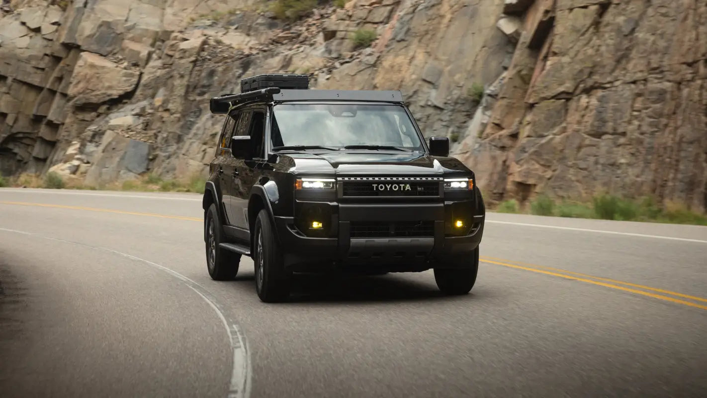2024 Toyota Land Cruiser driving on a mountain road, featuring The Atlas roof rack for secure and stylish cargo storage.