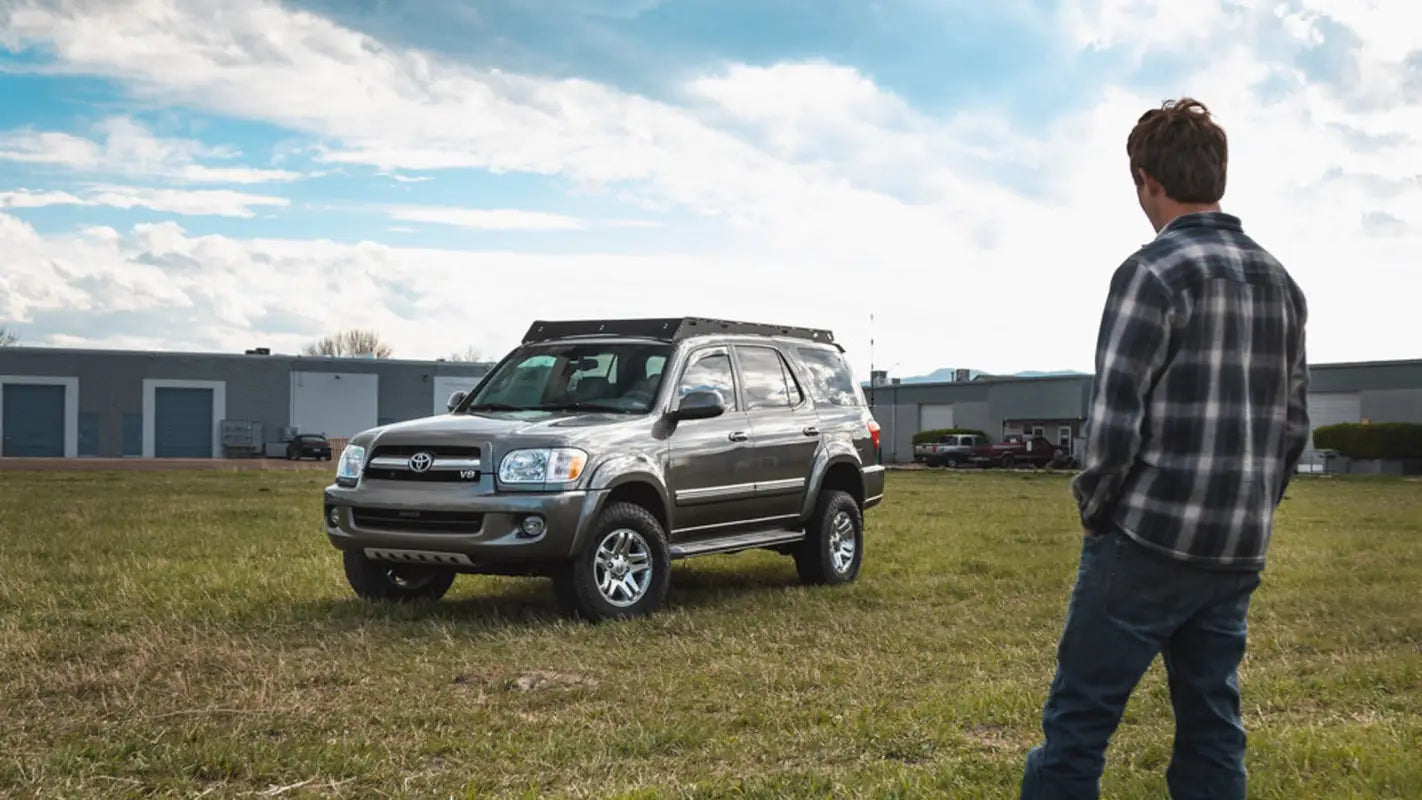A man observing a silver 2001-2007 Toyota Sequoia equipped with the Belford roof rack, set in an outdoor environment.