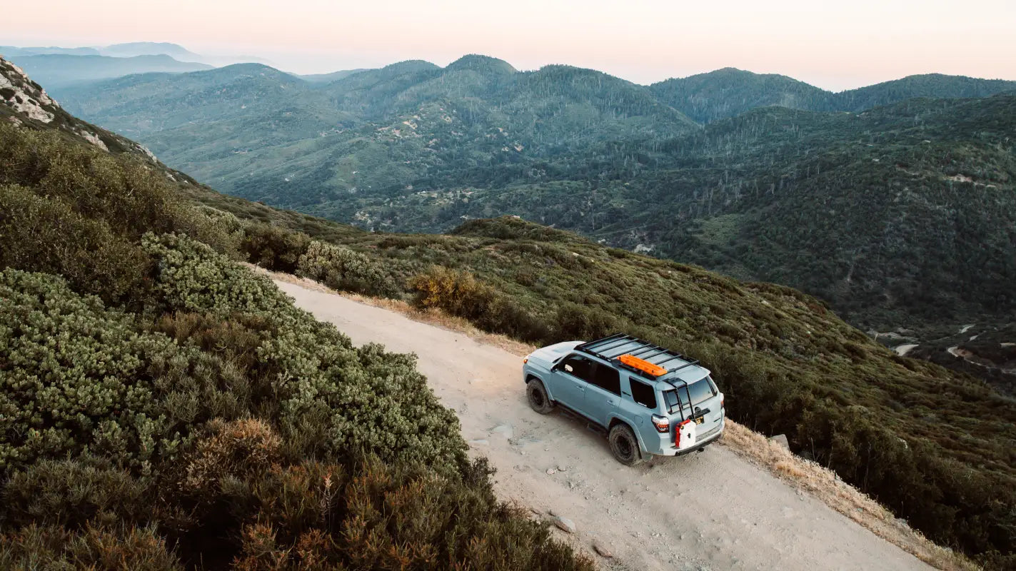 Light blue SUV with The Crestone roof rack on a mountain road, showcasing a full-length aluminum roof rack