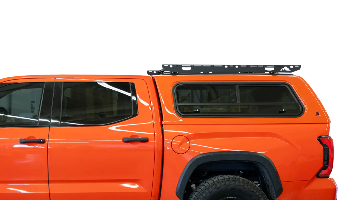 Close-up side view of an orange truck showcasing the Crow’s Nest topper rack installed on the roof for efficient cargo storage.