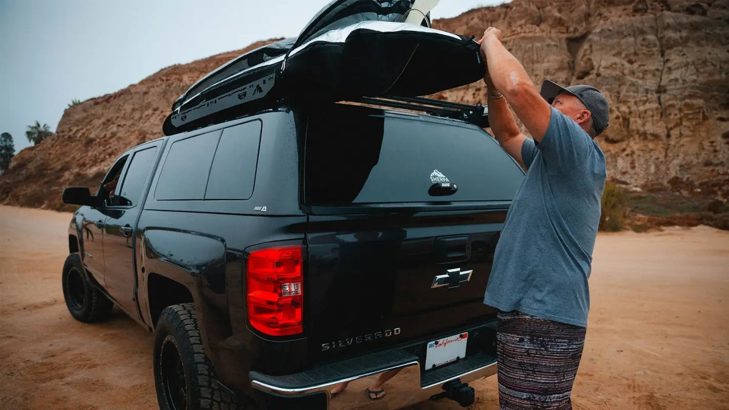 Man accessing gear stored on the Crow’s Nest topper rack installed on a black truck, highlighting its practical design for outdoor use.