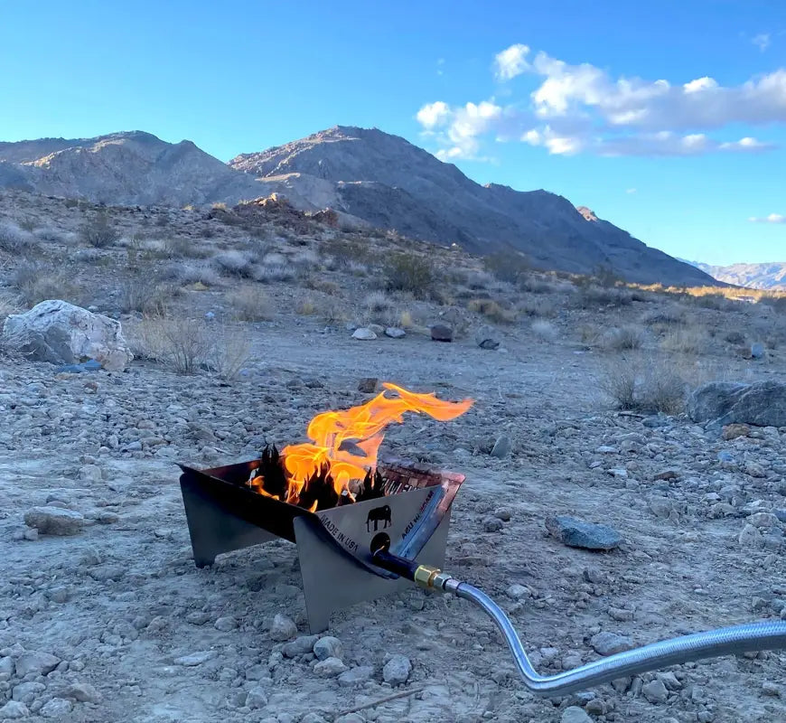 TemboTusk Fire Pit in use outdoors with flames burning, set against a scenic desert mountain backdrop, ideal for camping and overlanding.