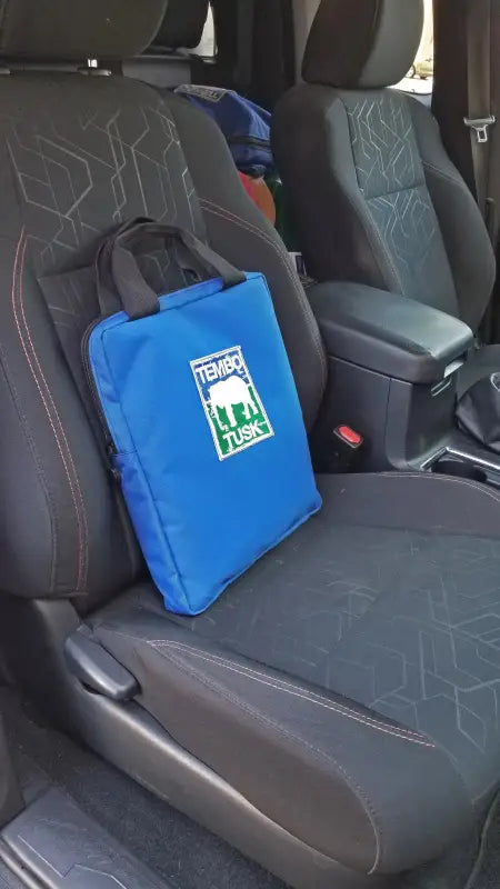 TemboTusk Fire Pit in its blue carry bag, conveniently placed on a car seat, showcasing its travel-friendly and compact design.