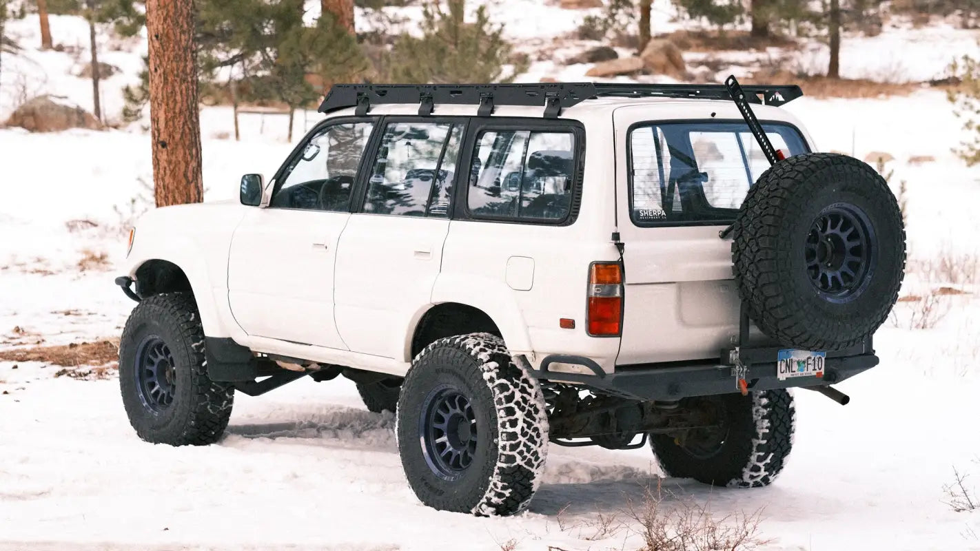 White 80 Series Land Cruiser with the La Sal roof rack, off-road tires, and rear-mounted spare tire in a snowy landscape.