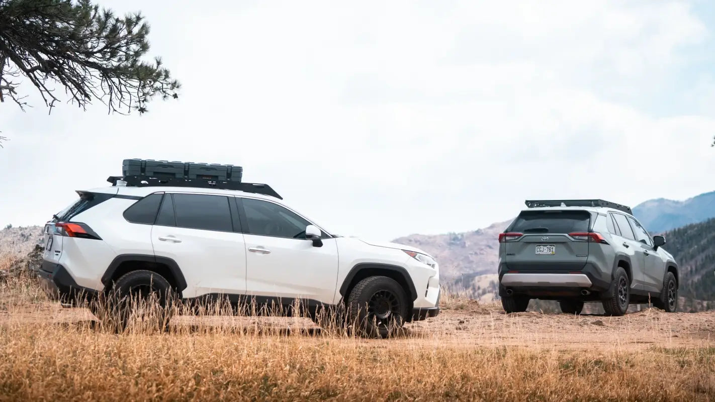 Two RAV4 vehicles equipped with The Snowmass roof racks parked in a scenic mountain area, showcasing rugged design and functionality.