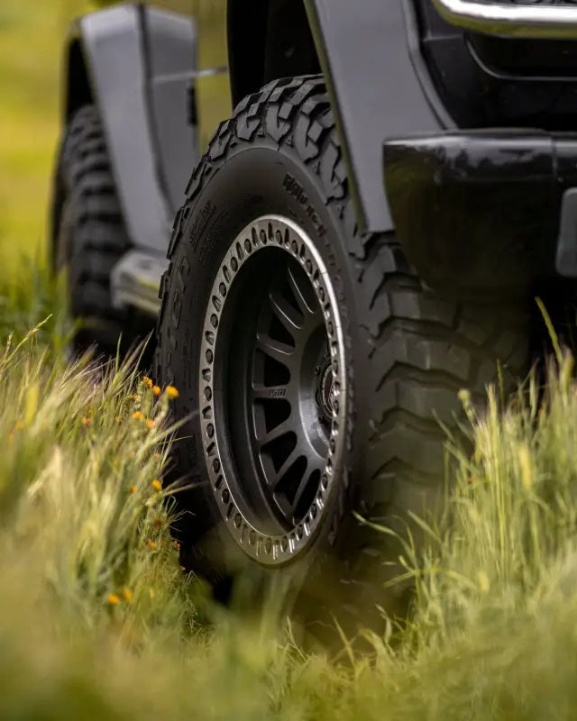 True Beadlock Ring for Hybrid Wheels V2 mounted on a vehicle tire in grassy terrain, emphasizing off-road capability and style.