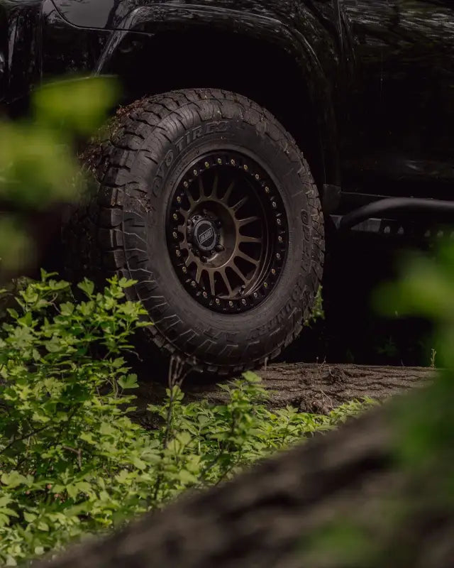 True Beadlock Ring for Hybrid Wheels V2 installed on an off-road vehicle tire in a forest setting, highlighting rugged design.