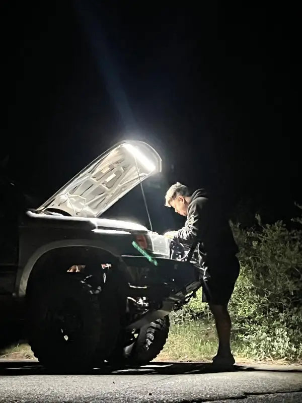 Person working under the hood of a vehicle at night, illuminated by a bright under hood LED light for enhanced visibility.