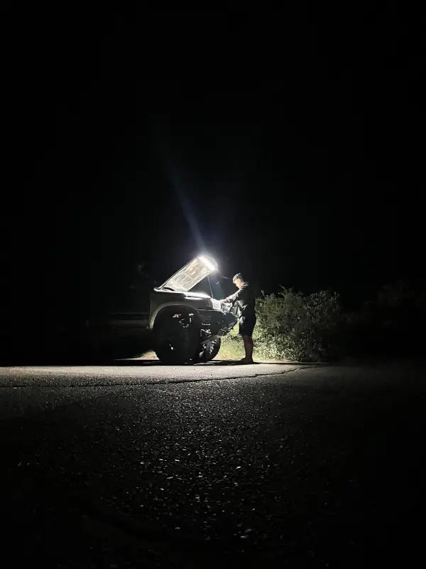 Person working on a vehicle at night, illuminated by the bright under hood LED light kit for enhanced visibility and convenience.