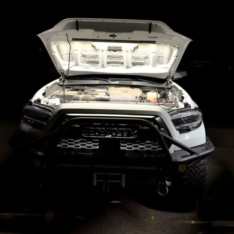 Toyota truck with its hood open, showcasing the bright illumination of the under hood LED light kit in a dark environment.