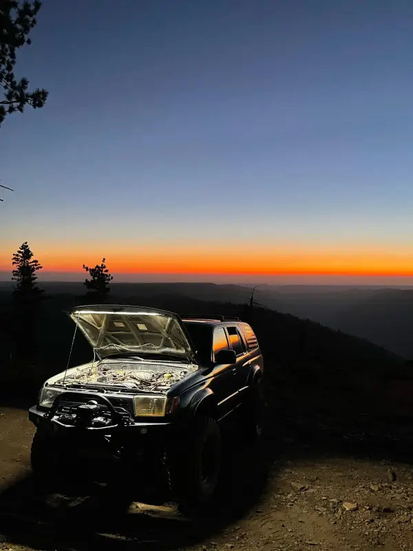 Toyota SUV with an illuminated engine bay using an under hood LED light kit, set against a scenic sunset backdrop.