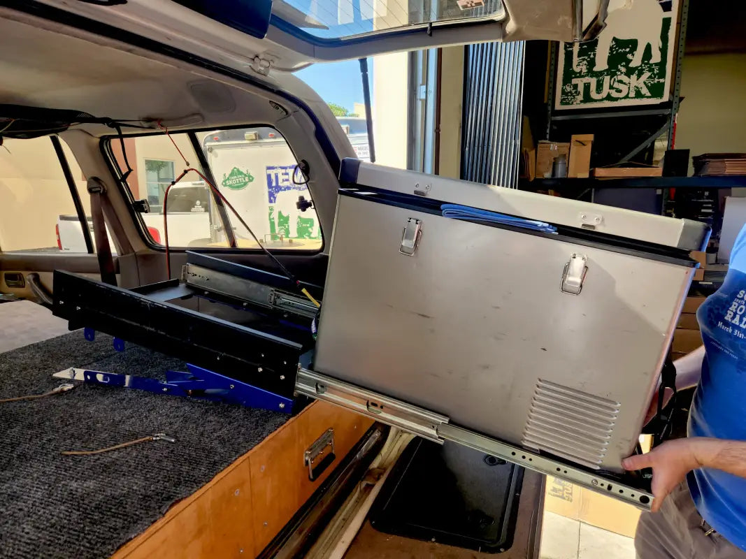 Fridge tilted on the Universal Tilt Slide Adapter inside a vehicle, demonstrating its adjustable angle for easy access during camping.