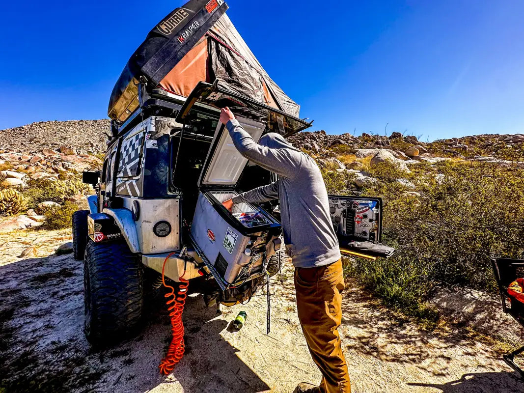 Outdoor camping scene with a rooftop tent and a fridge on the Universal Tilt Slide Adapter, emphasizing its utility in overland setups.