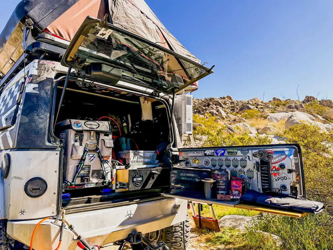 Overland camping setup featuring a Universal Tilt Slide Adapter, fridge, and organized storage in a rugged outdoor environment.
