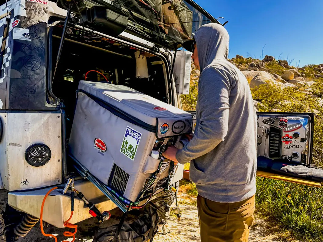 Camper adjusting a fridge mounted on the Universal Tilt Slide Adapter, showcasing its ease of use and compatibility with camping gear.