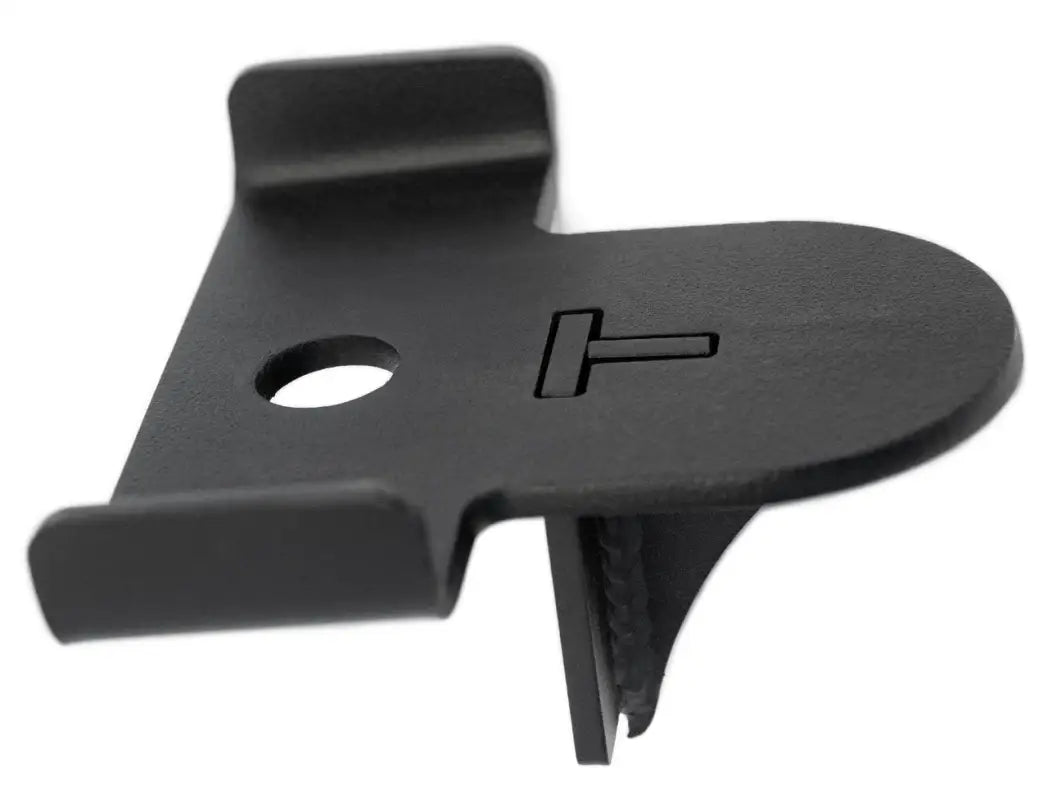 Angled view of a black steel strike plate with a center hole and 'T' engraving, included in the Tacoma bolt-on bump stop kit.