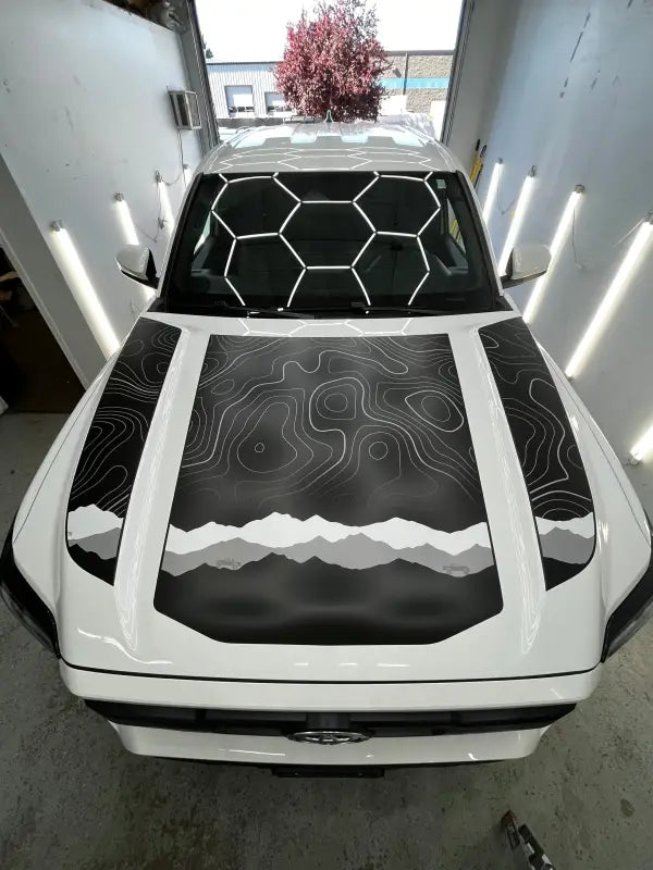 White car with mountain-themed apex hood stamp decal on 2024 Tacoma Apex Hood Stamp