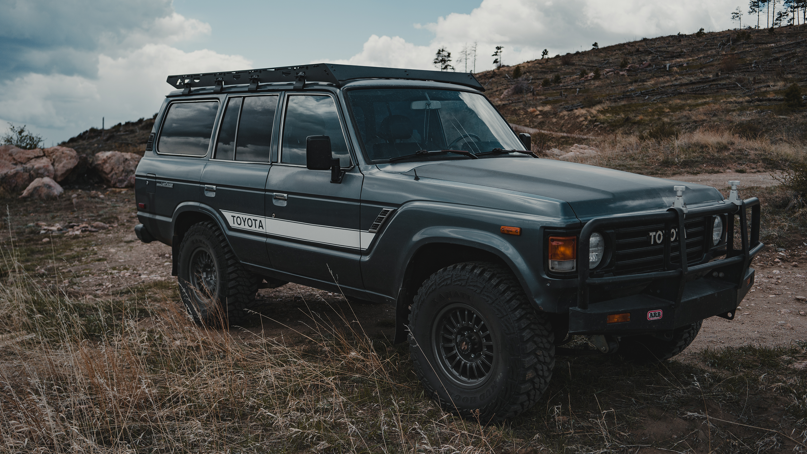 Toyota Land Cruiser 60 Series with a rugged roof rack parked in a mountainous terrain, ideal for outdoor gear transport and off-road use.