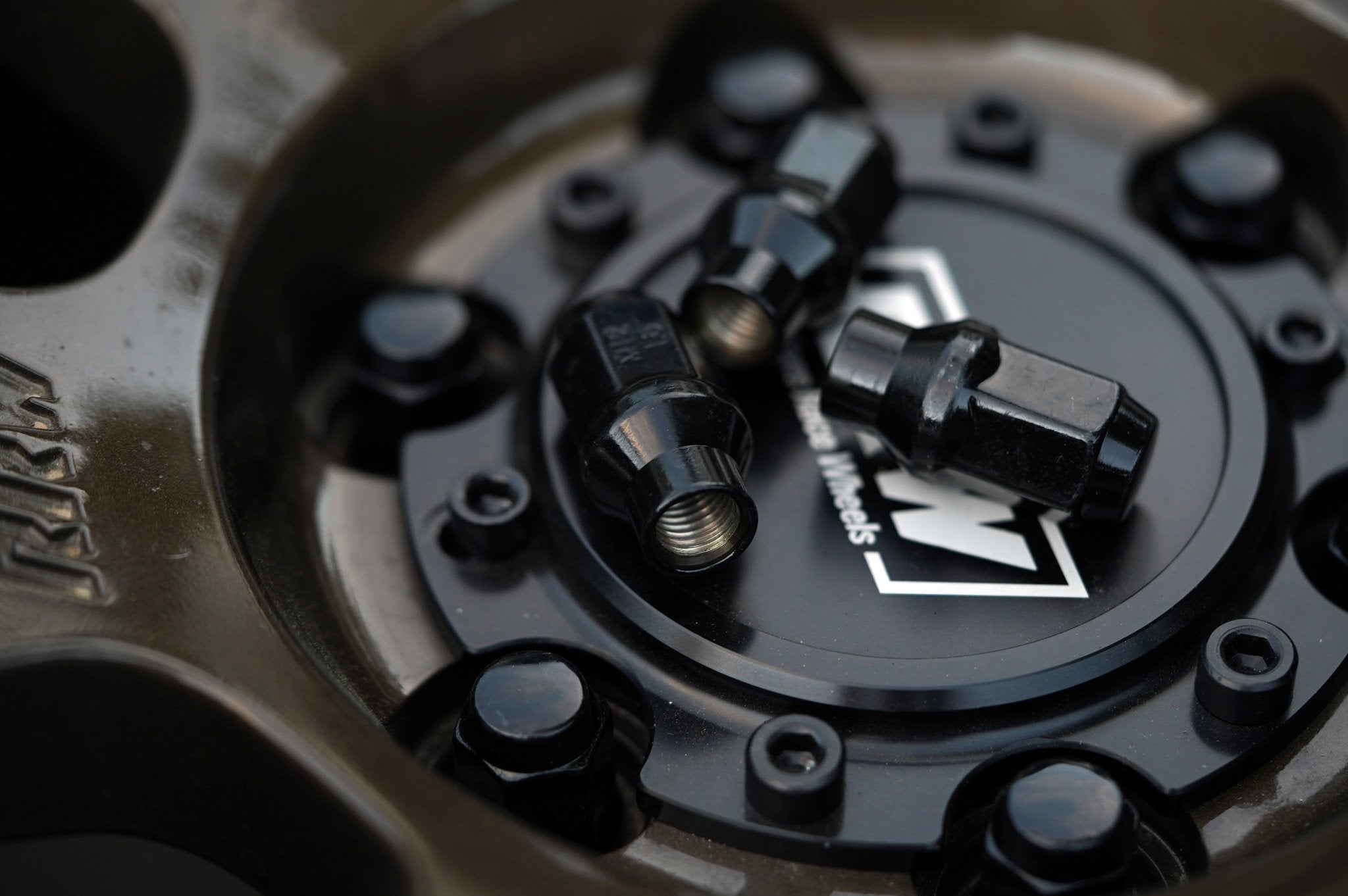 Three black hex lug nuts displayed on an RRW wheel center cap, showcasing their anti-corrosion finish and secure threading.