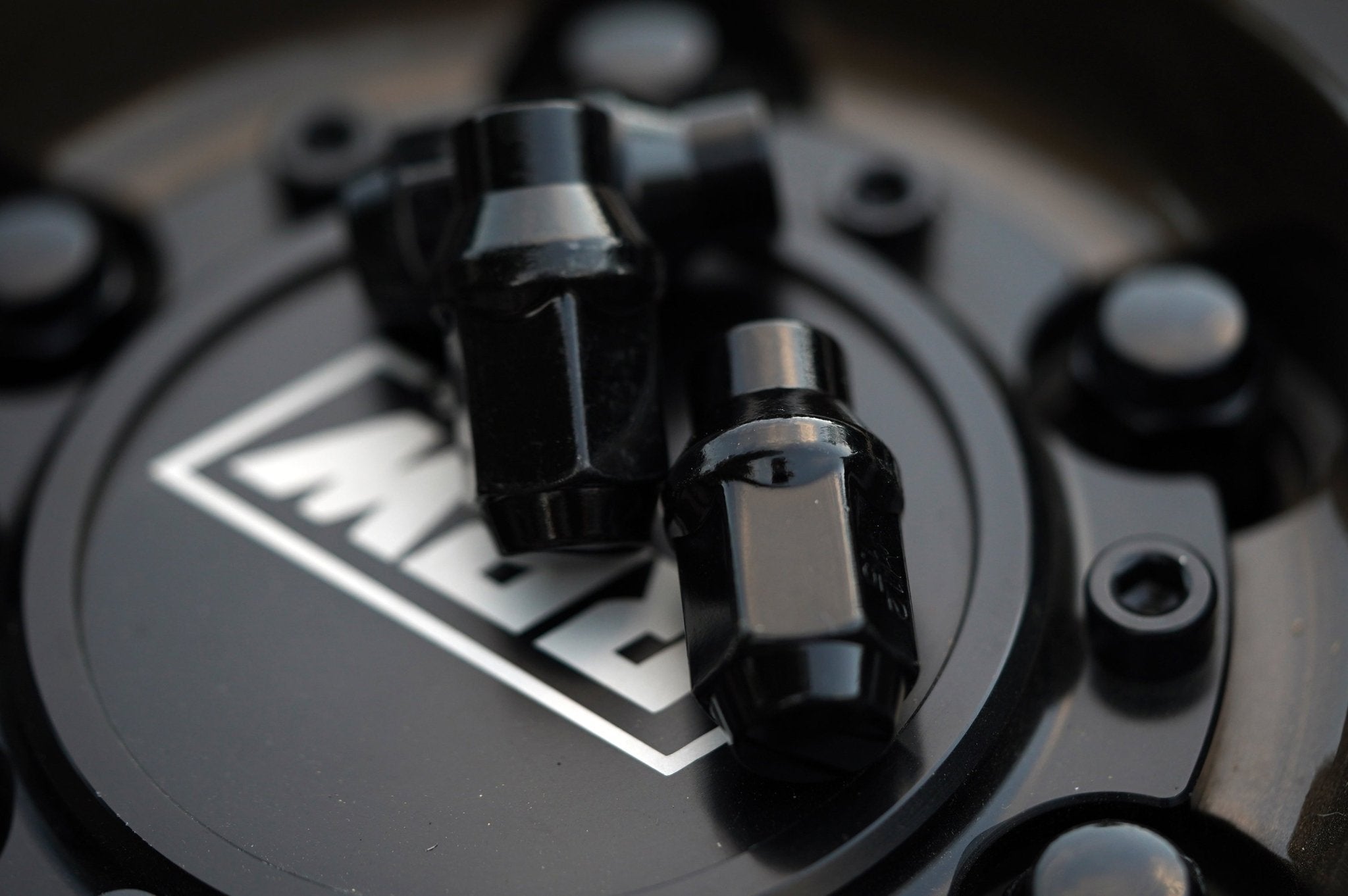 Black hex lug nuts displayed on an RRW wheel center cap, emphasizing their sleek design and compatibility with various vehicle models.