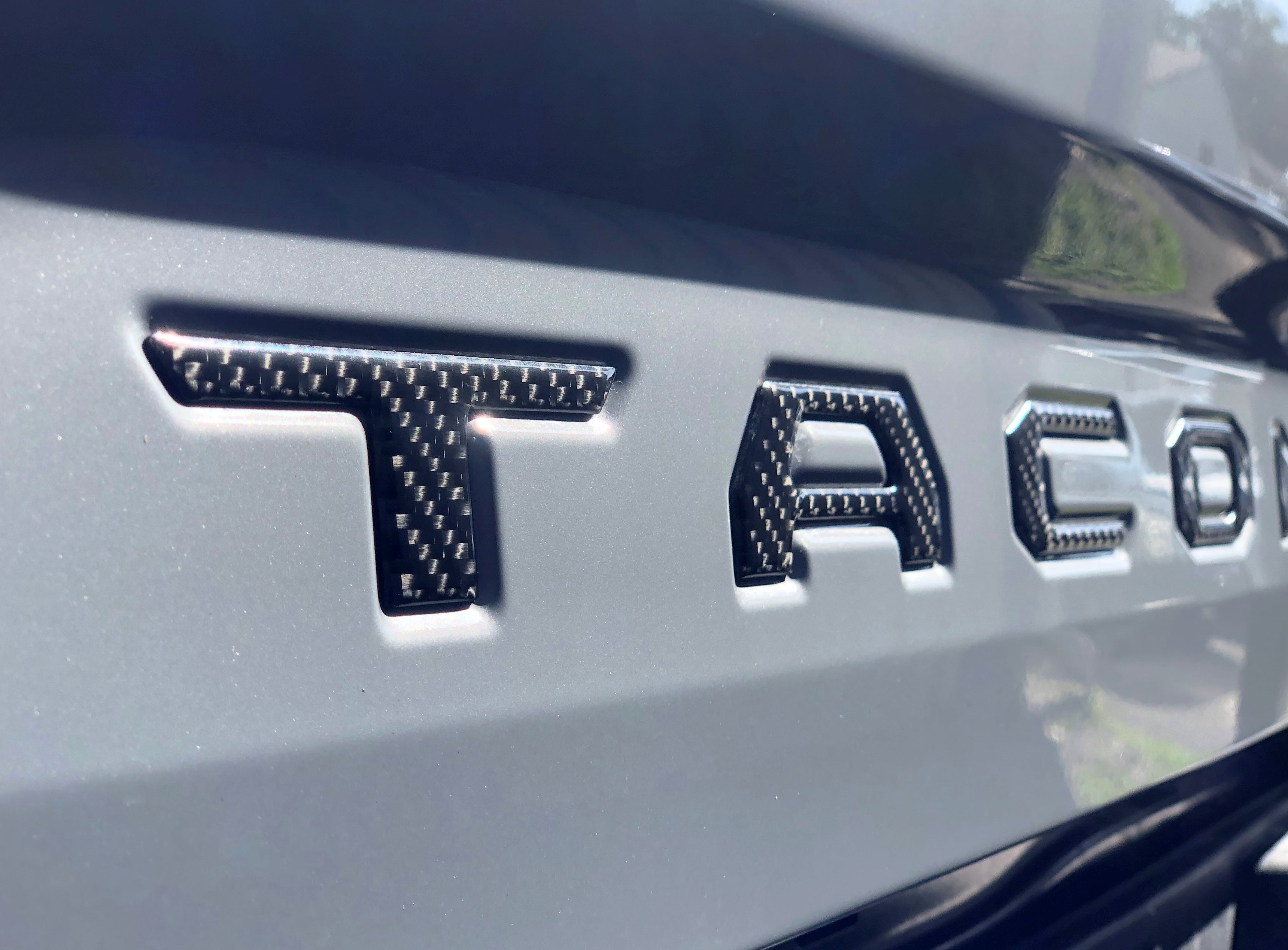 Angled view of carbon fiber tailgate letter inserts on a 2016-2023 Toyota Tacoma, emphasizing a premium finish.