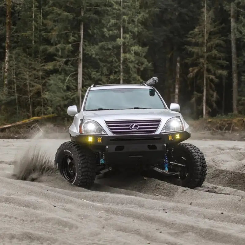 Lexus GX470 with long travel suspension and off-road tires driving on sandy terrain, showcasing its rugged build.