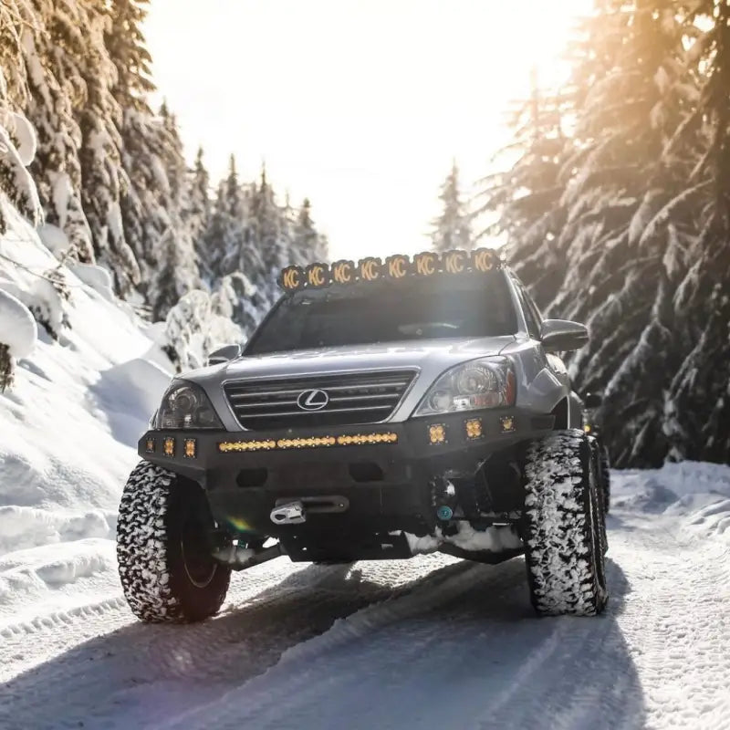 Lexus GX470 equipped with a long travel suspension kit, off-road tires, and KC lights driving through a snowy forest.