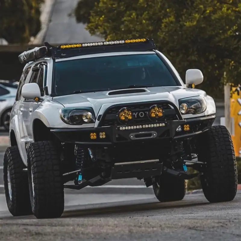 White 4th Gen 4Runner with +4.5 long travel suspension kit, off-road modifications, and LED lights on a rugged trail.