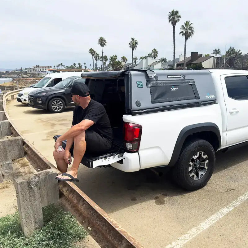 Man sitting on a truck tailgate with the CAP Mid-Size 5' Bed Air-Topper installed, demonstrating its practicality and ease of use.