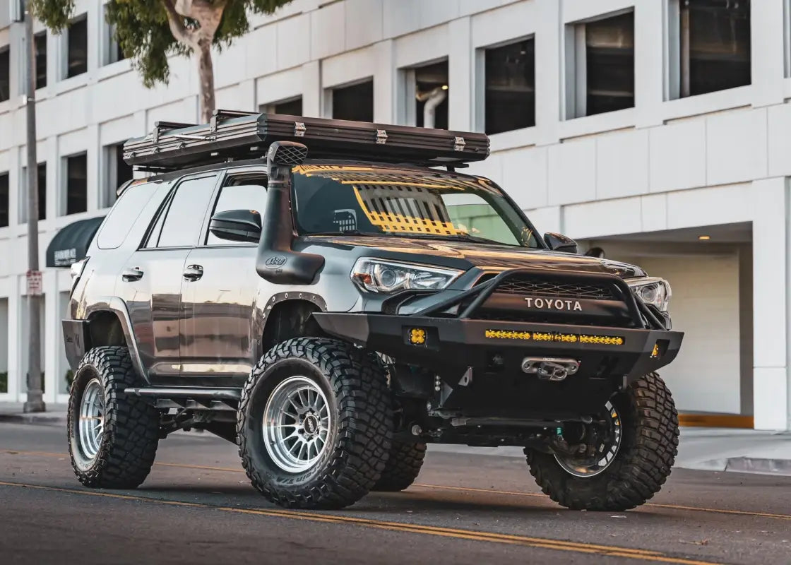 Lifted Toyota 4Runner equipped with DAKAR machined silver wheels, off-road tires, and roof rack, parked on a city street.