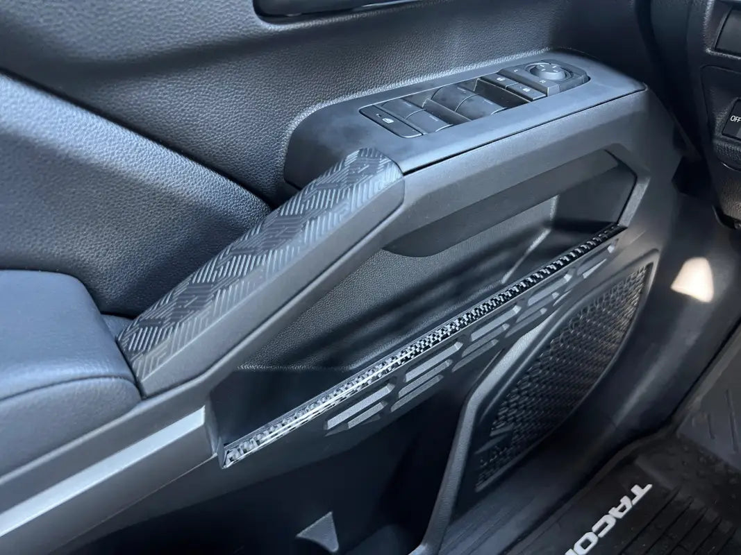 Close-up of installed door storage line accent trim on a 2024-2025 Toyota Tacoma, highlighting the textured carbon fiber finish.