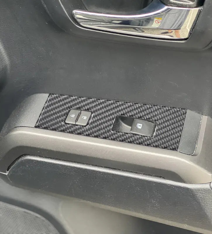 Installed carbon fiber door switch panel accent overlay on a Toyota Tacoma, showcasing a sleek and durable interior upgrade.