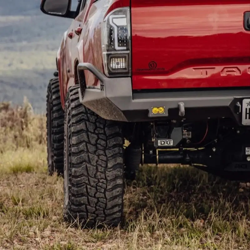 Close-up of DRT high clearance rear bumper on a red Toyota Tacoma, showcasing recovery points and off-road tires.