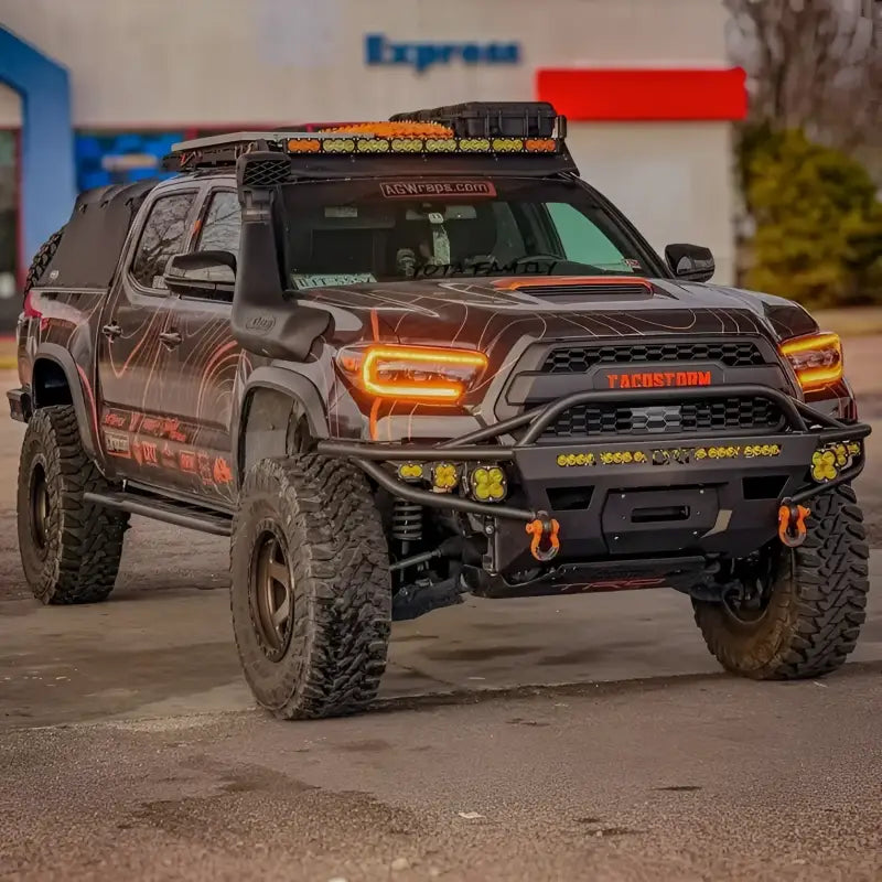 Black 2016-2023 Toyota Tacoma with DRT Hybrid Front Bumper, custom graphics, off-road lights, and winch in an urban setting.